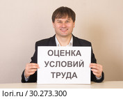 Сотрудник с табличкой "Оценка условий труда" за столом в офисе. Стоковое фото, фотограф Гетманец Инна / Фотобанк Лори