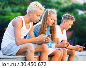 Three children keened on mobile phones during joint walk around city. Стоковое фото, фотограф Яков Филимонов / Фотобанк Лори