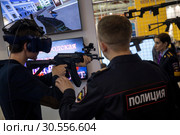 Сотрудник полиции помогает посетителю на тренажере виртуальной реальности для спецслужб на стенде Нижегородской академии МВД на Московском международном салоне образования на ВДНХ ЭКСПО в городе Москве, Россия (2019 год). Редакционное фото, фотограф Николай Винокуров / Фотобанк Лори