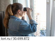 Взрослая женщина подсматривает за соседями в окно в бинокль из комнаты. Стоковое фото, фотограф Кекяляйнен Андрей / Фотобанк Лори