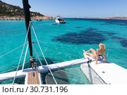 Woman relaxing on a summer sailing cruise, sitting on a luxury catamaran near picture perfect white sandy beach on Spargi island in Maddalena Archipelago, Sardinia, Italy. Стоковое фото, фотограф Matej Kastelic / Фотобанк Лори