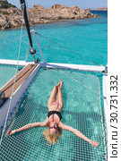 Woman relaxing on a summer sailing cruise,lying in hammock of luxury catamaran near picture perfect white sandy beach on Spargi island in Maddalena Archipelago, Sardinia, Italy. Стоковое фото, фотограф Matej Kastelic / Фотобанк Лори