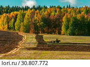 Трактор пашет землю в поле у леса. Стоковое фото, фотограф Евгений Горбунов / Фотобанк Лори