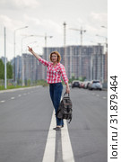 Middle age Caucasian woman waving hand for stop the car, standing on the median strip line of urban road. Стоковое фото, фотограф Кекяляйнен Андрей / Фотобанк Лори