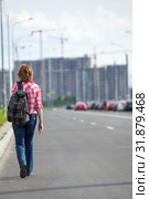 Rear view at woman hitchhiker walking on asphalt road in urban street, copyspace. Стоковое фото, фотограф Кекяляйнен Андрей / Фотобанк Лори