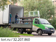 Рабочие перегружают новые пластиковые окна из одной грузовой машины в другую, специально оборудованную для перевозки стеклопакетов (2019 год). Редакционное фото, фотограф Наталья Николаева / Фотобанк Лори