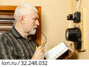 The man takes the readings of the apartment electric meter and writes it in the notebook. Стоковое фото, фотограф Акиньшин Владимир / Фотобанк Лори