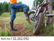 Man rider standing near dirt motorcycle in countryside, steps with boot on bike peg. Стоковое фото, фотограф Кекяляйнен Андрей / Фотобанк Лори