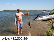 Только что пойманного сазана мужчина держит на кукане на фоне Волги летним днём (2019 год). Редакционное фото, фотограф Игорь Низов / Фотобанк Лори