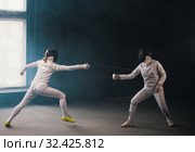 A fencing training in the studio - two women in protective costumes having a duel - pointing swords at each other. Стоковое фото, фотограф Константин Шишкин / Фотобанк Лори