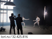 A fencing training in the studio - two women in protective costumes having a duel - two cameramans standing near the tripod and shooting the duel. Стоковое фото, фотограф Константин Шишкин / Фотобанк Лори