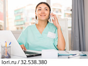 Practicioner woman in medical uniform talking by phone at laptop. Стоковое фото, фотограф Яков Филимонов / Фотобанк Лори