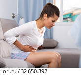 Young female at sofa holding hands on the illness stomache. Стоковое фото, фотограф Яков Филимонов / Фотобанк Лори
