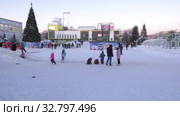 Дети катаются с ледяной горки на городской площади. Children ride on an ice slide in the town square. (2019 год). Редакционное видео, видеограф Евгений Романов / Фотобанк Лори