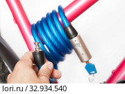 Human hand holding cable lock for bicycle fastening to a fixed bike rack, white background. Стоковое фото, фотограф Кекяляйнен Андрей / Фотобанк Лори