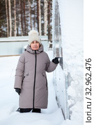 Mature woman standing in snowdrift next to door of her plastic greenhouse on backyard of country house. Стоковое фото, фотограф Кекяляйнен Андрей / Фотобанк Лори