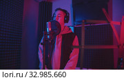 A man in headphones rapping through the pop-filter in the microphone - recording his track in the studio - music stand on the foreground. Стоковое видео, видеограф Константин Шишкин / Фотобанк Лори