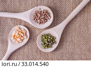 Three wooden spoons with cereals buckwheat, mung beans and peas on burlap on the table, top view. Стоковое фото, фотограф Катерина Белякина / Фотобанк Лори