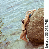 Beautiful slim young woman in a black bikini swimsuit resting on a rocky beach (2016 год). Стоковое фото, фотограф katalinks / Фотобанк Лори