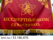 Мужчина держит красный баннер с надписью "Бессмертный полк Севастополь" перед началом шествия Бессмертный полк в центре города Севастополя, Крым (2019 год). Редакционное фото, фотограф Николай Винокуров / Фотобанк Лори