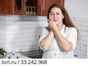 Young woman with toothache standing in kitchen, holding her cheek with hands. Стоковое фото, фотограф Кекяляйнен Андрей / Фотобанк Лори