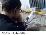 Молодой мужчина-стеклодув выдувает стеклянный шарик в мастерской на фабрике ёлочных игрушек в поселке Крестцы Новгородской области (2019 год). Редакционное фото, фотограф Румянцева Наталия / Фотобанк Лори