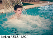 Young man having fun with the water in the swimming pool. Happy young man having fun and relaxing under a water jet at swimming pool. Стоковое фото, фотограф Evgenii Mitroshin / Фотобанк Лори