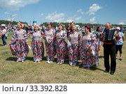 Хор пожилых женщин в цветастых платьях поют рядом с гармонистом на поляне, на музыкальном фестивале Каратаг. Красноярский край. (2019 год). Редакционное фото, фотограф Светлана Попова / Фотобанк Лори