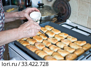 Пожилая женщина смазывает горячие пирожки маслом с помощью кулинарной кисточки. An elderly woman in the kitchen greases hot cakes with oil using a cooking brush. Стоковое фото, фотограф Владимир Литвинов / Фотобанк Лори