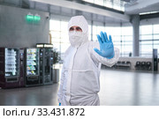 Epidemiologist in a protective suit shows a prohibition gesture against the waiting room at the airport or train station. Стоковое фото, фотограф Евгений Харитонов / Фотобанк Лори