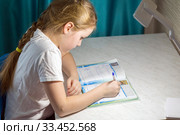 An adorable little schoolgirl sits at a desk and does homework in her room. Стоковое фото, фотограф Акиньшин Владимир / Фотобанк Лори