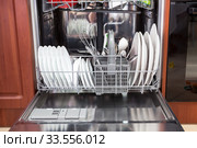 Opened silver dishwasher with clean plates, spoons and cups is in the kitchen, front view. Стоковое фото, фотограф Кекяляйнен Андрей / Фотобанк Лори