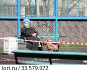Пожилая женщина в медицинской маске отдыхает на лавочке в дни самоизоляции при коронавирусе COVID-19. Хабаровская улица. Район Гольяново. Город Москва. Россия (2020 год). Редакционное фото, фотограф lana1501 / Фотобанк Лори