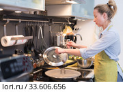 Stay at home housewife woman cooking in kitchen, stir frying dish in a saucepan, preparing food for family dinner. Стоковое фото, фотограф Matej Kastelic / Фотобанк Лори