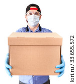 Caucasian delivery man wearing plastic glasses, medical mask and blue neoprene gloves giving cardboard, isolated on a white background. Стоковое фото, фотограф Кекяляйнен Андрей / Фотобанк Лори