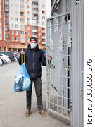 Taking out the trash during Covid-19 pandemic, person wearing medical mask holding blue drawtape garbage bag. Стоковое фото, фотограф Кекяляйнен Андрей / Фотобанк Лори