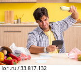 Young man calculating expences for vegetables in kitchen. Стоковое фото, фотограф Elnur / Фотобанк Лори