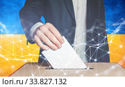 Мужчина избиратель опускает бюллетень в урну для голосования на фоне украинского флага. Стоковое фото, фотограф Сергей Тиняков / Фотобанк Лори
