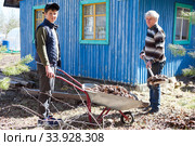Portrait of senior father and preteen son at work together, man loading dried leaves in wheelbarrow from ground with shovel. Стоковое фото, фотограф Кекяляйнен Андрей / Фотобанк Лори