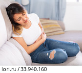 Mexican female at sofa holding hands on the illness stomache. Стоковое фото, фотограф Яков Филимонов / Фотобанк Лори