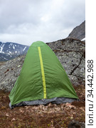 Green waterproof and windproof tent for hiking is in mountains at windy weather, standing behind big stone for protection from the wind. Стоковое фото, фотограф Кекяляйнен Андрей / Фотобанк Лори