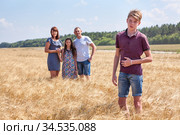 Concept of adopted kid, boy standing on foreground with adoptive family on background, stepson with dad, mom and preteen sister. Стоковое фото, фотограф Кекяляйнен Андрей / Фотобанк Лори