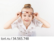 Funny little girl wearing eyeglasses imitates a strict teacher against white background. Стоковое фото, фотограф Nataliia Zhekova / Фотобанк Лори