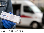 Волонтер держит коробку с тривалентной вакциной "Гриппол Плюс" на фоне специального автомобиля скорой помощи мобильного пункта бесплатной вакцинации от гриппа на Тверской улице у метро в центре города Москвы, Россия (2020 год). Редакционное фото, фотограф Николай Винокуров / Фотобанк Лори