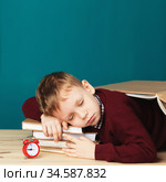 tired school boy asleep on books. little student sleeping on textbooks. Child in school uniform lies on the table with big pile of books against blue wall. Eyes closed. School concept. Стоковое фото, фотограф Nataliia Zhekova / Фотобанк Лори