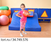 Пятилетняя девочка стоит с мячом в руках на фоне гимнастической горки. Стоковое фото, фотограф Ирина Борсученко / Фотобанк Лори