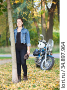Attractive Caucasian woman biker with a motorcycle is in a park or forest at autumn season, full length portrait. Стоковое фото, фотограф Кекяляйнен Андрей / Фотобанк Лори