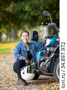 Female motorcycle rider with white crash helmet in hand sitting near her blue bike. Стоковое фото, фотограф Кекяляйнен Андрей / Фотобанк Лори