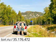 a man and a woman autotourists stand on the highway near the car and point to the high mountain Aleksandrovskaya Sopka on a sunny summer day. Стоковое фото, фотограф Акиньшин Владимир / Фотобанк Лори
