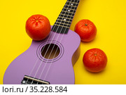 Фрагмент четырехструнной гитары укулеле на желтом фоне с мандаринами. Стоковое фото, фотограф V.Ivantsov / Фотобанк Лори